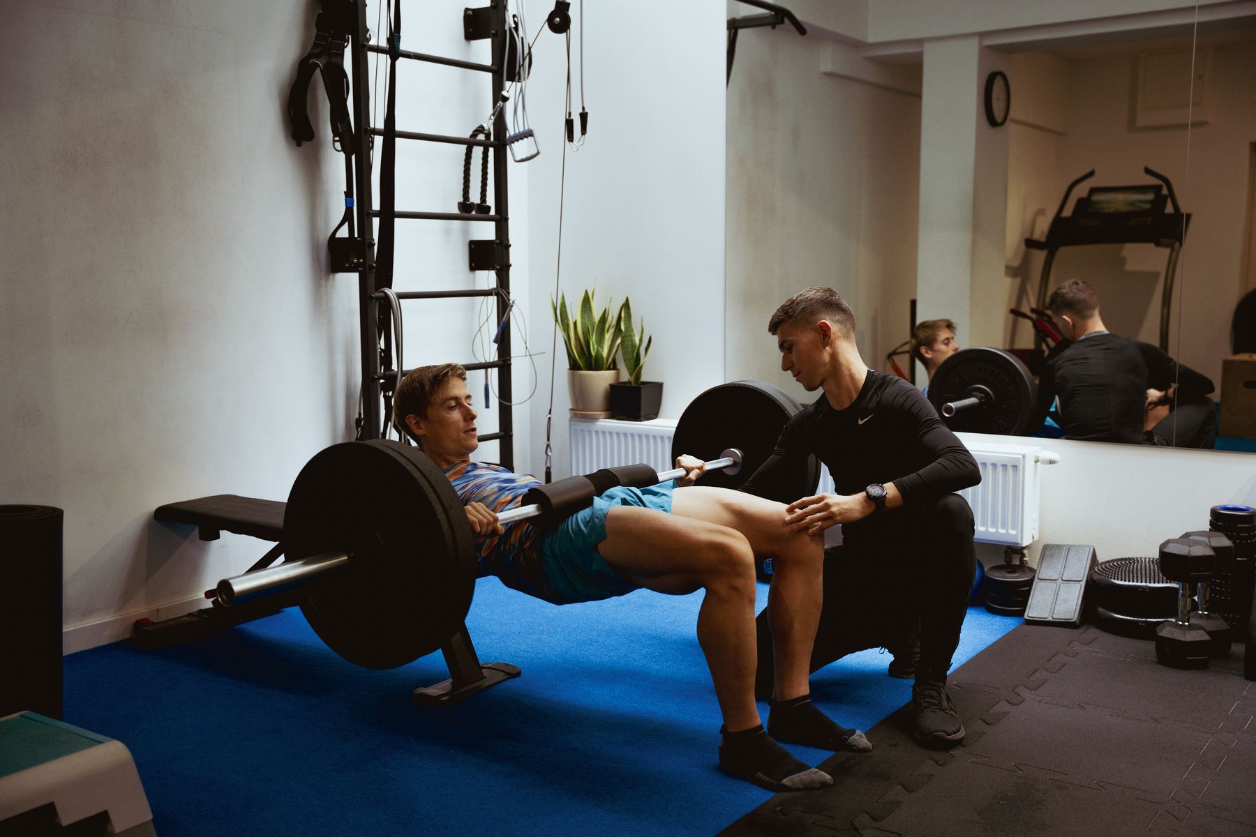 Biegacz wykonuje hip thrust ze sztangą pod okiem trenera